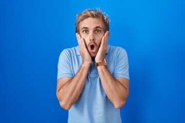Caucasian man standing over blue background afraid and shocked, surprise and amazed expression with...
