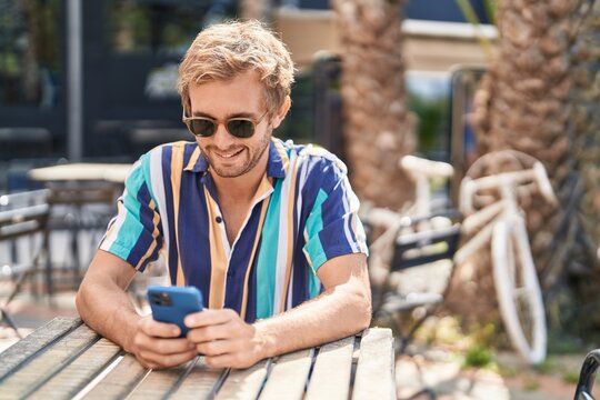 Young man tourist using smartphone sitting on table at coffee shop terrace