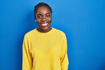 Beautiful black woman standing over blue background with a happy and cool smile on face. lucky person.