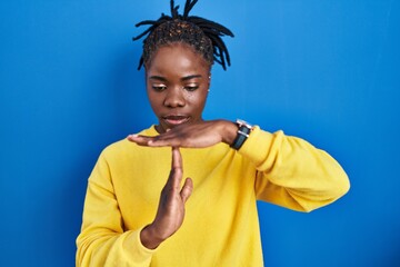 Beautiful black woman standing over blue background doing time out gesture with hands, frustrated...