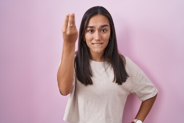 Young hispanic woman standing over pink background doing italian gesture with hand and fingers confident expression