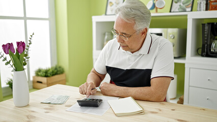 Middle age man with grey hair calculating expenses at dinning room