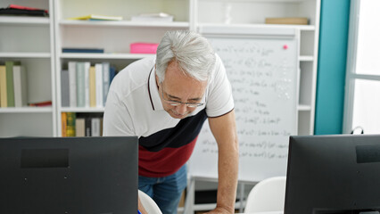 Fototapeta premium Middle age man with grey hair university teacher using computer at university classroom
