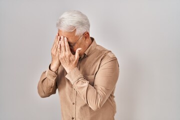 Hispanic senior man wearing glasses with sad expression covering face with hands while crying....