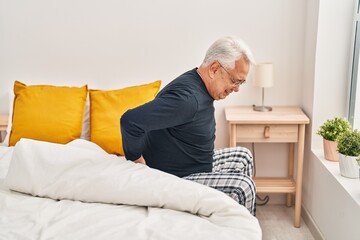 Fototapeta premium Senior man suffering for backache sitting on bed at bedroom