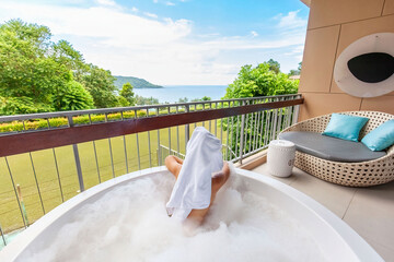 Woman indulges in a luxurious spa bathing experience with foam and organic skincare on terrace, enjoying the relaxing sea view. Back view.