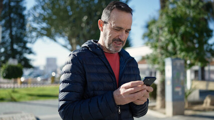 Middle age man smiling confident using smartphone at park