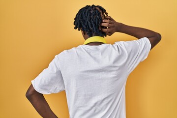 Young african man with dreadlocks standing over yellow background backwards thinking about doubt...