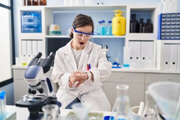 Hispanic girl with down syndrome working at scientist laboratory looking at the watch time worried, afraid of getting late