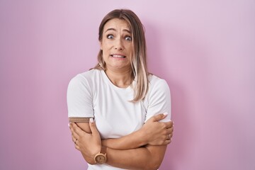 Fototapeta premium Blonde caucasian woman standing over pink background shaking and freezing for winter cold with sad and shock expression on face