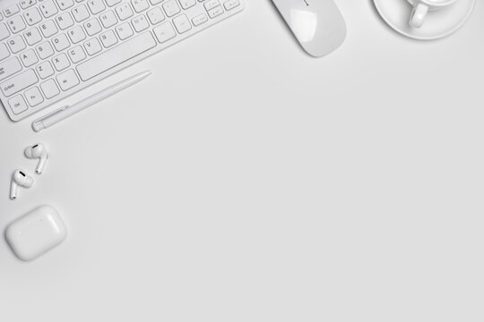 Total white workplace table with mouse, keyboard, headphones on white background with copy space.