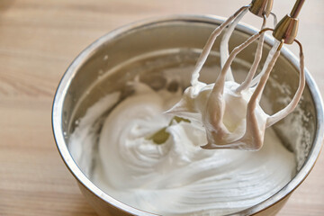 Fototapeta na wymiar Mixer beaters with whipped egg whites. Whipped egg whites and other ingredients for cream or as an ingredient for baking on wooden table, closeup