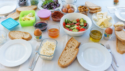 Turkish style breakfast ingredients on table: Tasty olives, cucumbers, jams, tomato sauces, cheeses, peppers, breads.