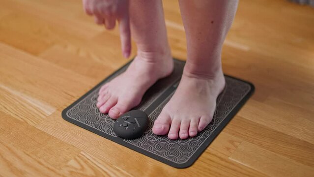Woman using ems foot massager pad. Acupuncture simulator for home use. Sweden. 