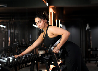 Fototapeta na wymiar Single Arm Dumbbell Exercise for Upper Back by Young Indian Fit Gym Girl in Black Sportswear