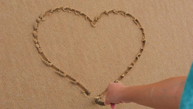 Girl drawing heart on sand with a stick.