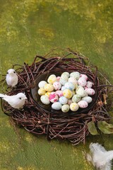 Sugar candy in the form of bird eggs on a glass plate in a wreath of branches on a green concrete background. Spring equinox day, the onset of spring, the arrival of birds concept.