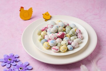 Sugar candy in the form of bird eggs on a white plate on a pink concrete background.