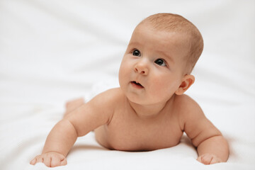 A newborn baby in a diaper is lying on stomach on a white background and looking to the side.