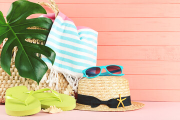 Green flip flops with straw hat, sunglasses, towel and monstera leaf on wooden background