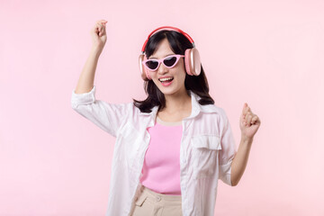 happy young asian woman model with stylish trendy sun glasses enjoy listening music by headphone audio and dancing isolated on pink studio background. technology, girl fashion, accessory concept.