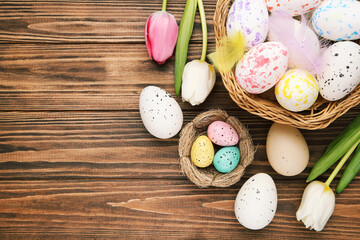Eggs in basket and nest, flowers of tulips on brown wooden background