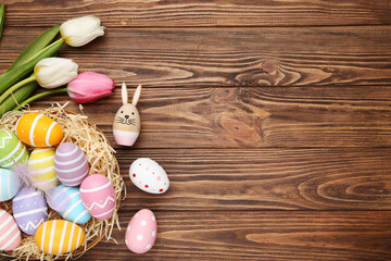 Colorful eggs in nest and flowers of tulips on brown wooden background