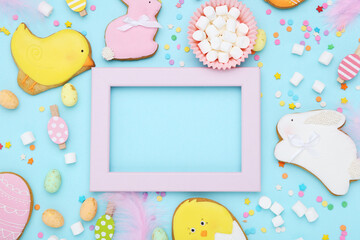 Wooden frame with cookies, marshmallows, eggs and sprinkles on blue background
