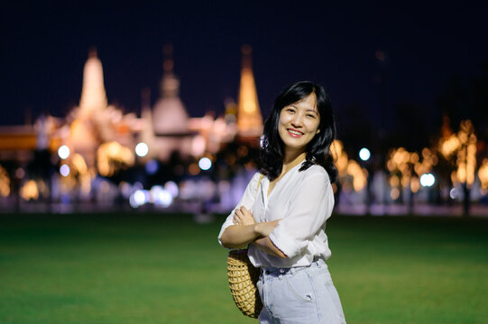 Portrait young beautiful asian woman smiling while travel at Temple of the Emerald Buddha or Wat Phra Kaew in night view point, Bangkok, Thailand.