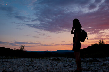 Fototapeta premium A silhouette of a female traveler standing in the mountains during sunset