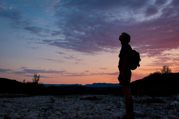 A silhouette of a female traveler standing in the mountains during sunset