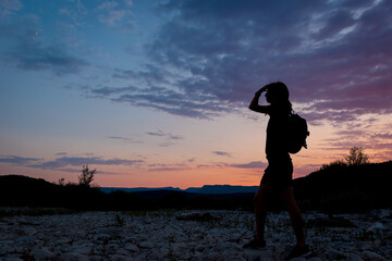 A silhouette of a female traveler standing in the mountains during sunset