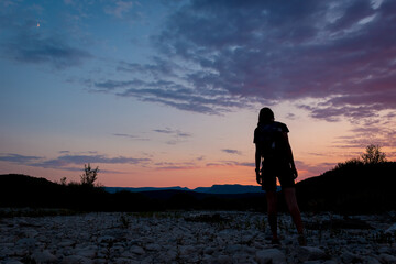 A silhouette of a female traveler standing in the mountains during sunset