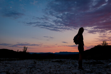 A silhouette of a female traveler standing in the mountains during sunset