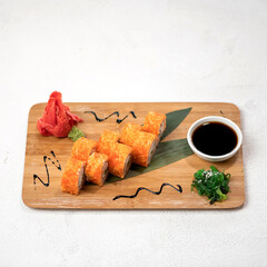 Set of sushi rolls with flying fish caviar tobiko on bamboo sheet and wooden board. Rolls with ginger, soy sauce and hiashi. Japanese food. White background. Top view. Copy space. 