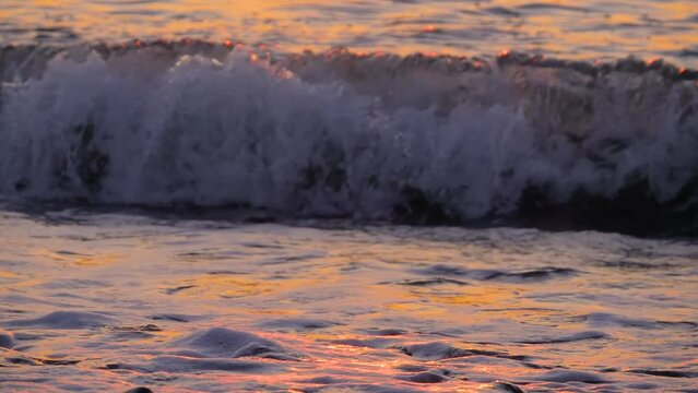 Slow motion - view of sea water waves are crashing on the pebble beach at sunset - close up view. Nature and relaxation concept