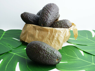 Close up. Tropical fruit, avocados in green leaves next to a kraft paper bag.