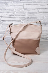 Women's beige bag with a long belt. Cross-body made of artificial leather. Gray and black background.
