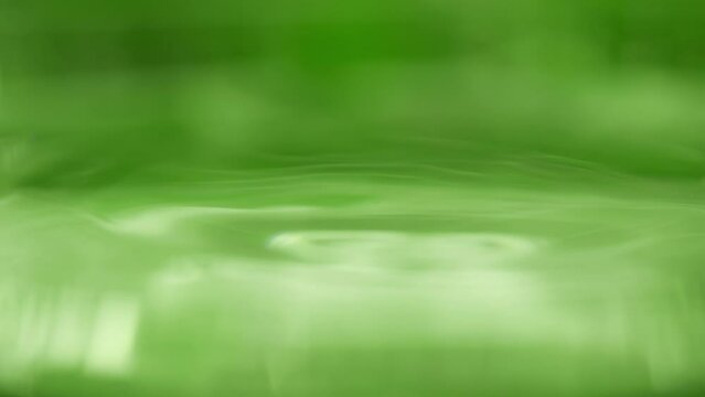 Drop is falling into green liquid. Crystal clear water splash. Concept of natural springs and wellness or beauty products. Green tea or aloe vera extract. Cold mineral water in slow motion