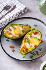 Egg baked in avocado sprinkled with bacon and herbs on a plate vertical view
