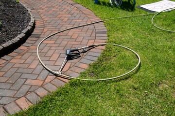 Hose attached to pressure washing wand and nozzle laying on a brick walkway