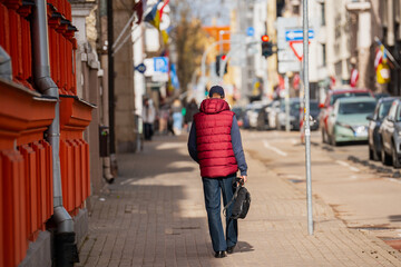 Man with red vest and a bag walking on the street side walk at sunny day