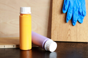 Two bottles of acrylic paint on a wooden table. Items needed for repair. Repair paints and rubber gloves