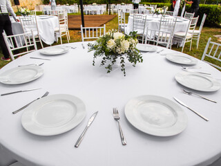Fototapeta premium Beautiful outdoor wedding decoration in city. Candles and dried flowers and accessories with bouquets and glasses on table with linen tablecloth on newlywed table on green lawn
