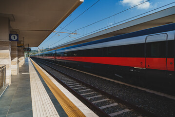 Naklejka premium Long train arrives at rural train station in Italy.