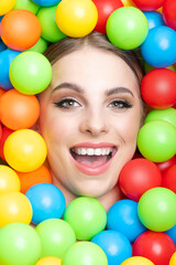 Fototapeta na wymiar Fashion, pop-art and make-up concept. Beautiful woman close-up studio portrait in colorful balls background. Model's head surrounded with various colors plastic balls. Girl looking at camera