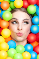 Fototapeta na wymiar Fashion, pop-art and make-up concept. Beautiful woman close-up studio portrait in colorful balls background. Model's head surrounded with various colors plastic balls. Girl looking away