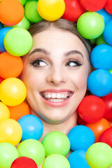 Fototapeta na wymiar Fashion, pop-art and make-up concept. Beautiful woman close-up studio portrait in colorful balls background. Model's head surrounded with various colors plastic balls. Girl looking away