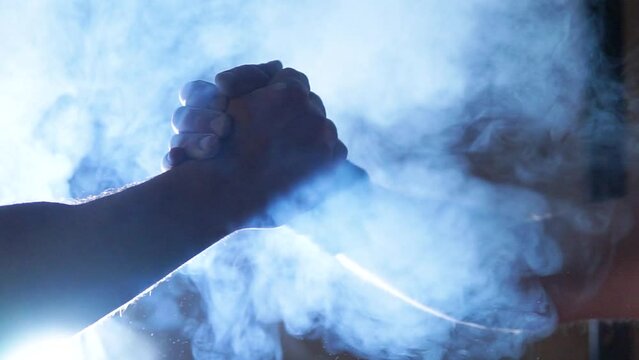 Strong with athletic body men greet and high-five each other close-up against the backdrop of light with smoke and magnesia in a dark gym, hands