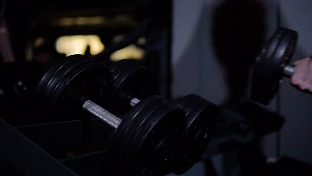 Strong with athletic body man takes a dumbbell in a dark gym, dumbbell close-up